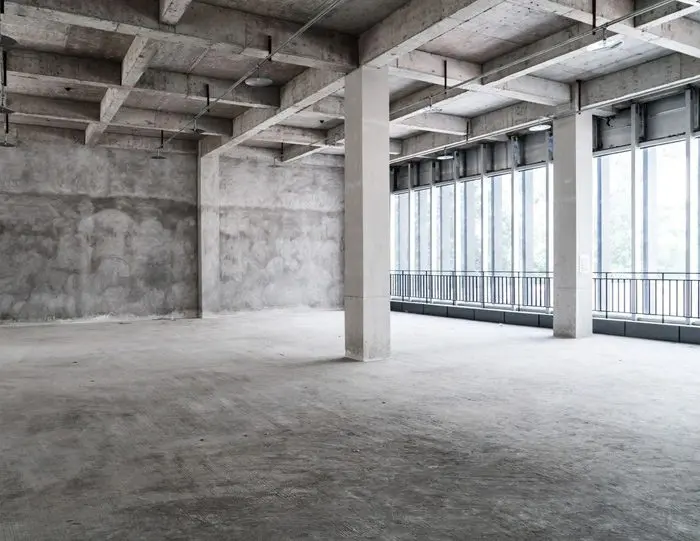 A large empty room with many windows and concrete floors.
